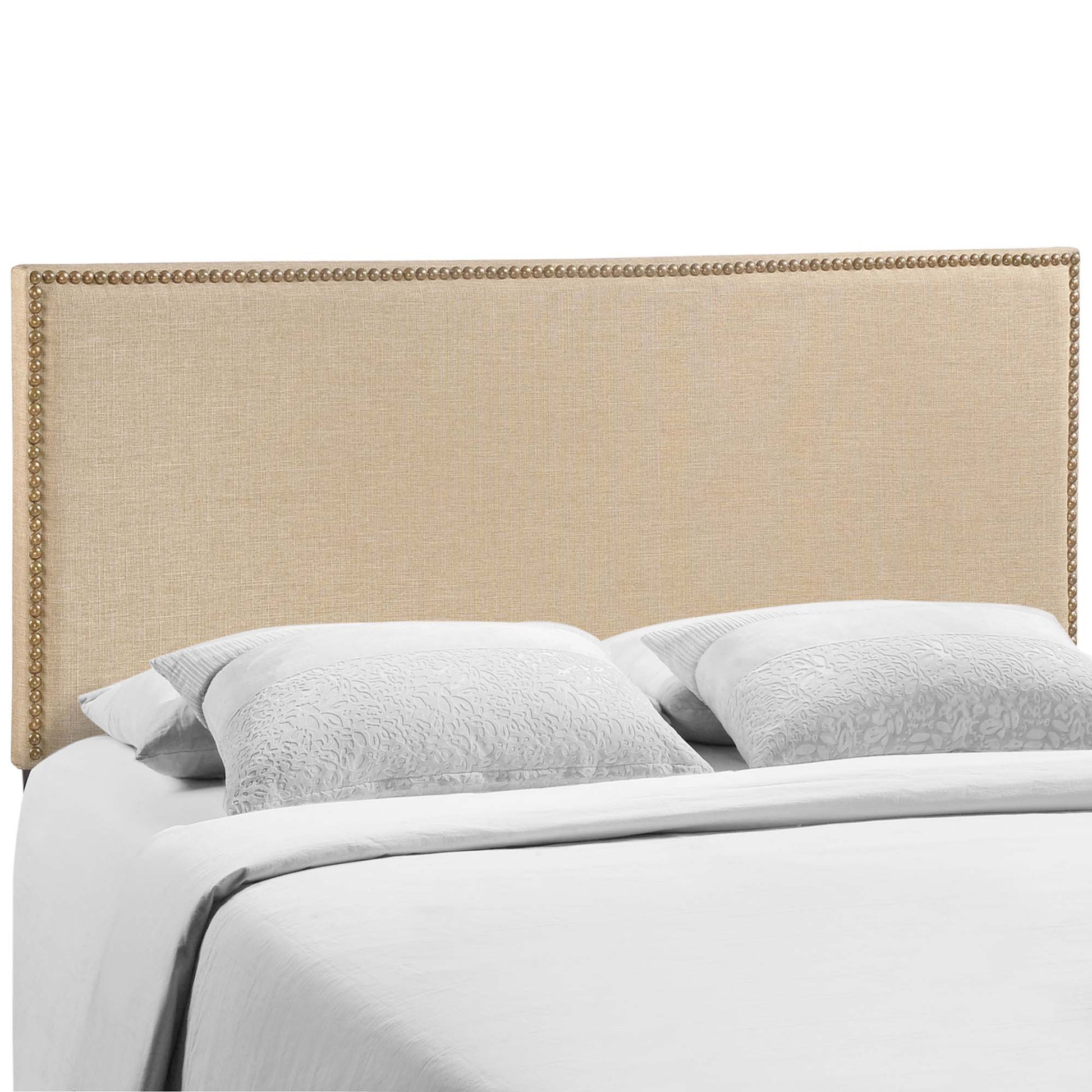 Beige upholstered headboard with gold nailhead trim atop a white bed with pale gray patterned pillows.