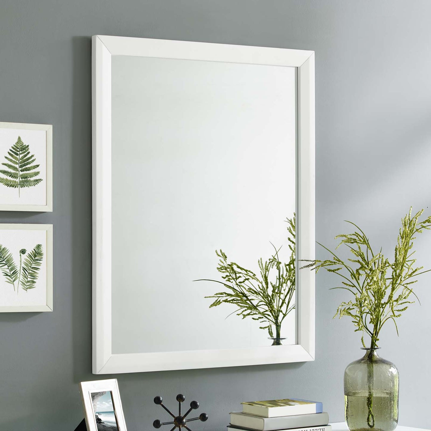 White rectangular wall mirror with beveled frame on gray wall; modern minimalist style with greenery vase nearby.