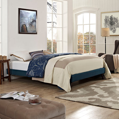 Azure fabric queen bed frame with beige duvet and navy patterned quilt in a bright, window-filled bedroom.