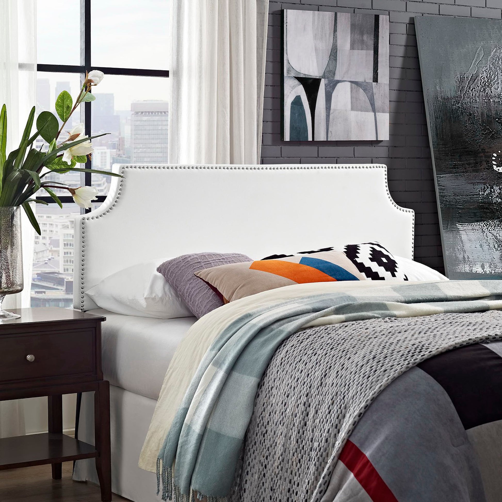 White upholstered vinyl queen headboard with curved nailhead trim; gray bedding and colorful pillows.