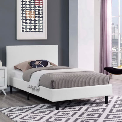 White upholstered platform bed with low headboard, gray quilted cover, beige & navy pillows, black legs, geometric rug.