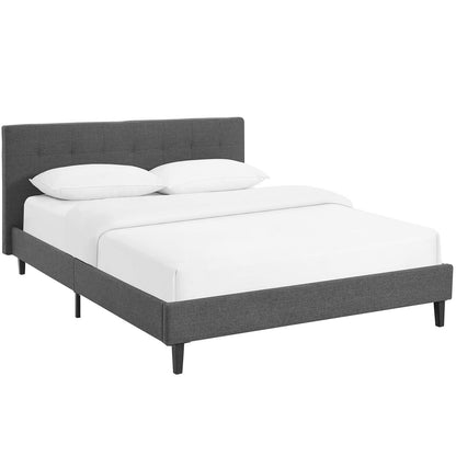 Gray upholstered platform bed with tufted headboard, low frame and black tapered legs, white bedding.