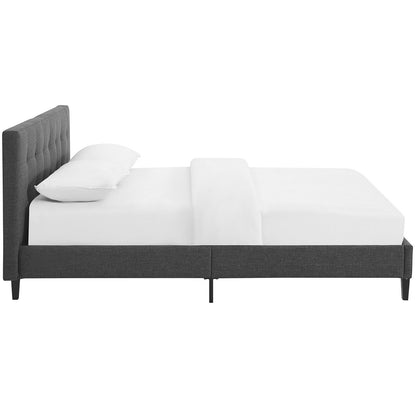 Gray fabric upholstered bed with tall tufted headboard, low platform, slim legs, shown with white bedding.