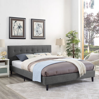 Gray upholstered platform bed with tufted headboard, cream/gray bedding & light blue throw; framed art, lamps, plant.