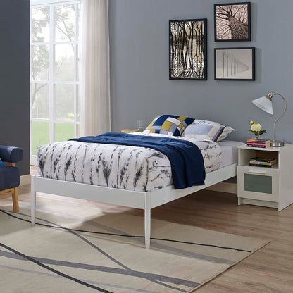 White platform twin bed frame with marble-pattern duvet, blue throw and geometric pillows; nightstand with lamp, framed art and beige rug.