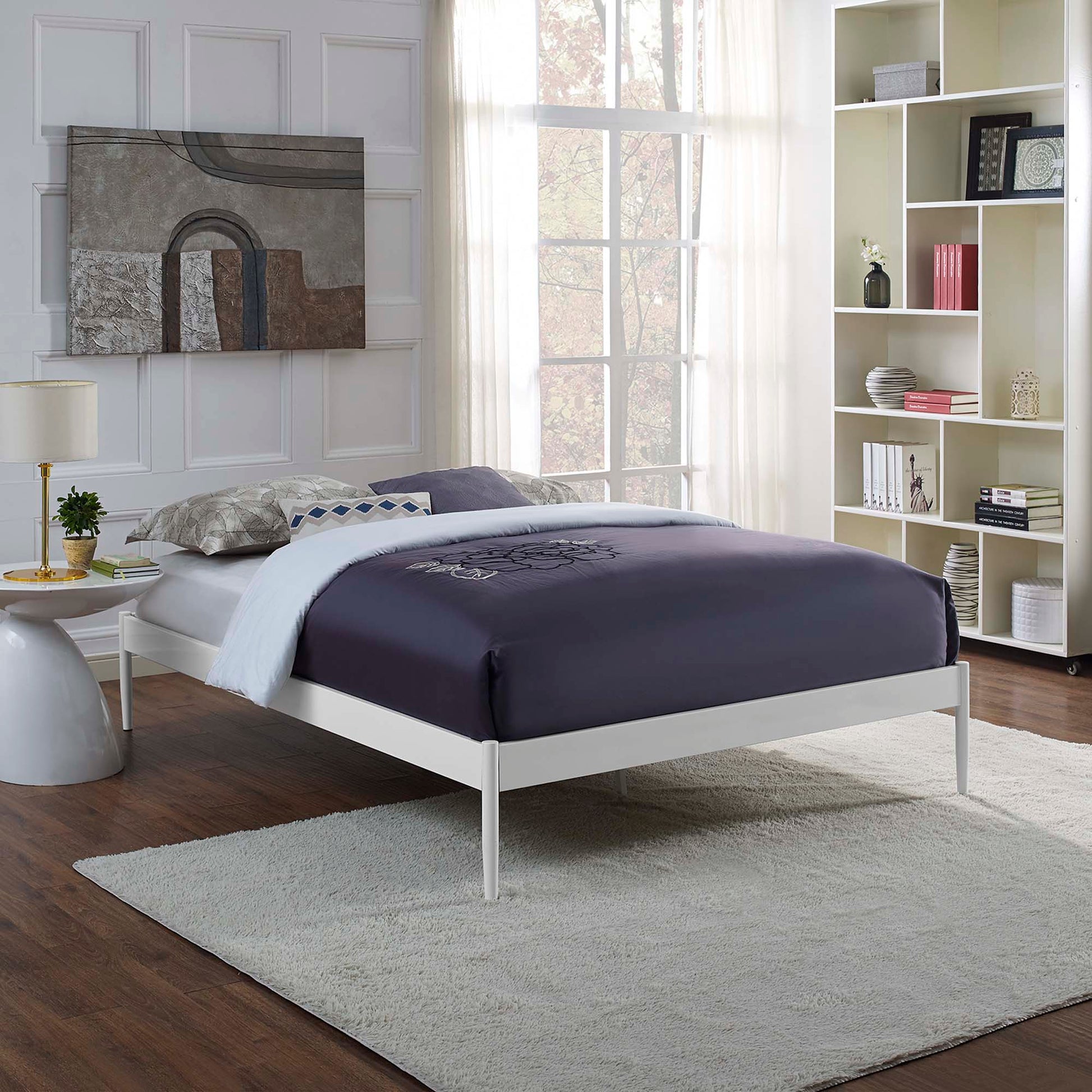 White metal full bed frame with a navy duvet, light gray rug, tall white bookshelf, and large gray abstract wall art.