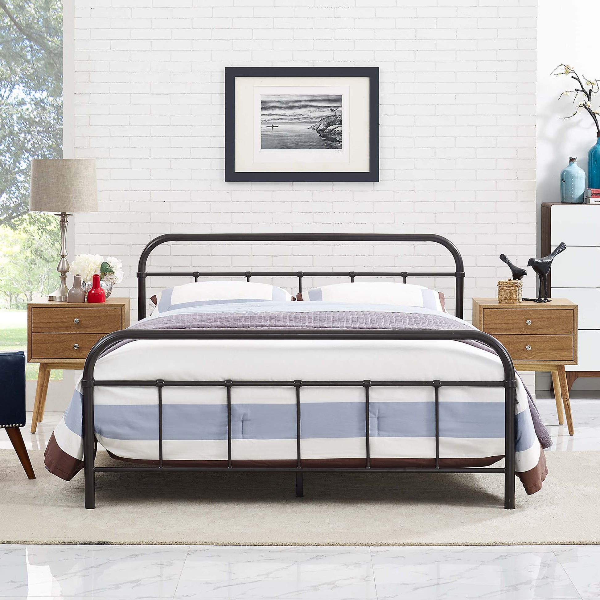 Stainless steel queen bed frame with arched headboard and footboard, blue-gray striped bedding, light wood nightstands, white brick wall.