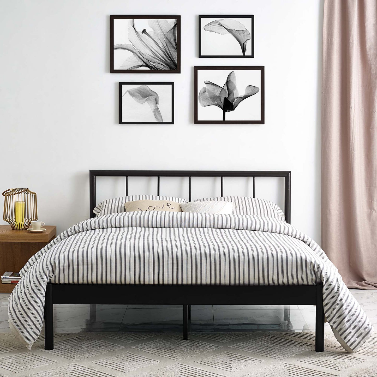 Black metal full bed frame with striped gray duvet, beige pillows, wooden nightstand, lantern lamp, and botanical prints on the wall.