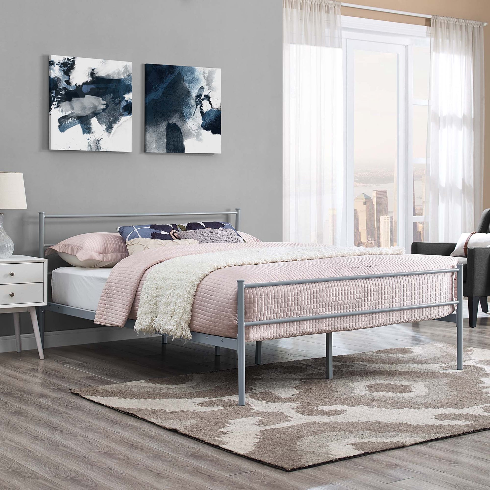 Gray metal platform bed with pink quilt, cream throw, gray walls, abstract navy art, nightstand, and rug in a modern bedroom.