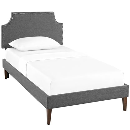 Gray fabric upholstered platform bed with curved nailhead-trim headboard, tapered wooden legs, white bedding.