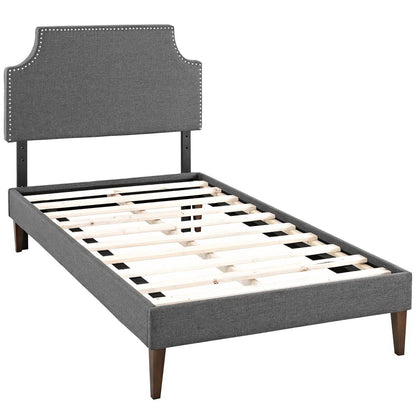 Gray fabric twin platform bed with curved, nailhead-trim headboard, slatted base, and squared tapered legs.