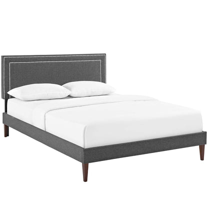 Grey upholstered platform bed with a padded studded headboard, white bedding, and tapered wood legs.