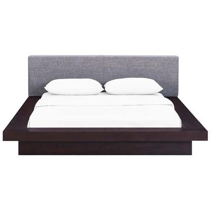 Low-profile platform bed with dark espresso wooden frame, gray fabric headboard, and white bedding with two pillows.