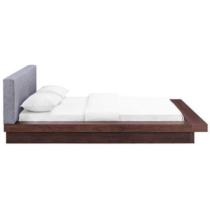 Gray fabric queen platform bed with upholstered headboard and white linens, low-profile frame with built-in side shelf.