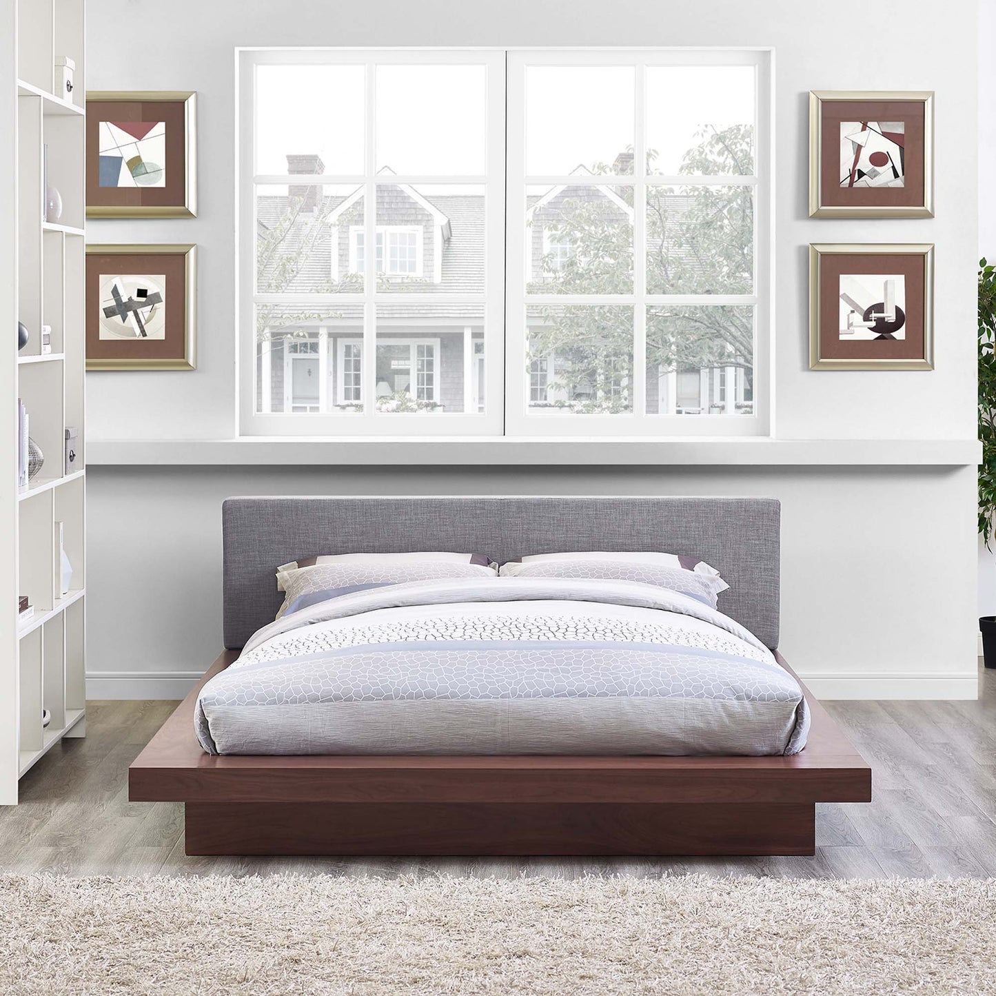 Low-profile platform bed with walnut wood base, gray upholstered headboard, and light gray bedding in a modern bedroom.