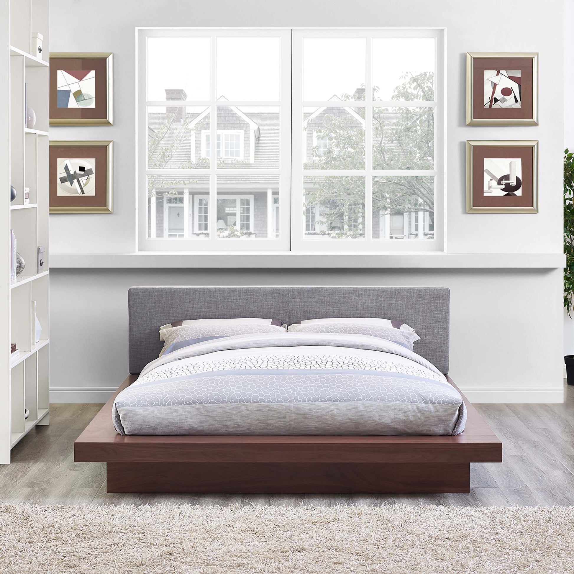 Low-profile platform bed with walnut wood base, gray upholstered headboard, and light gray bedding in a modern bedroom.