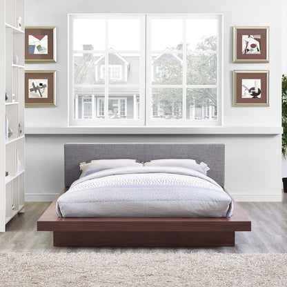 Low-profile platform bed with walnut wood base, gray upholstered headboard, and light gray bedding in a modern bedroom.