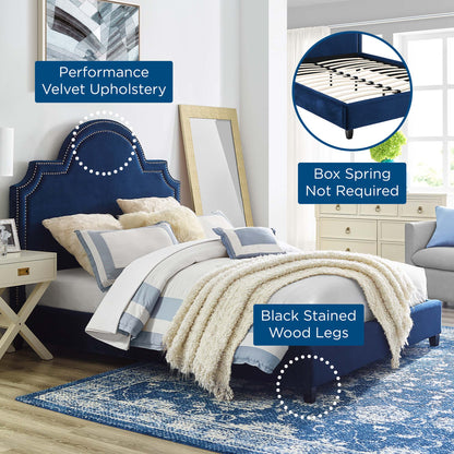 Navy blue velvet upholstered bed with studded headboard, black stained wood legs, white/blue bedding on a blue rug.