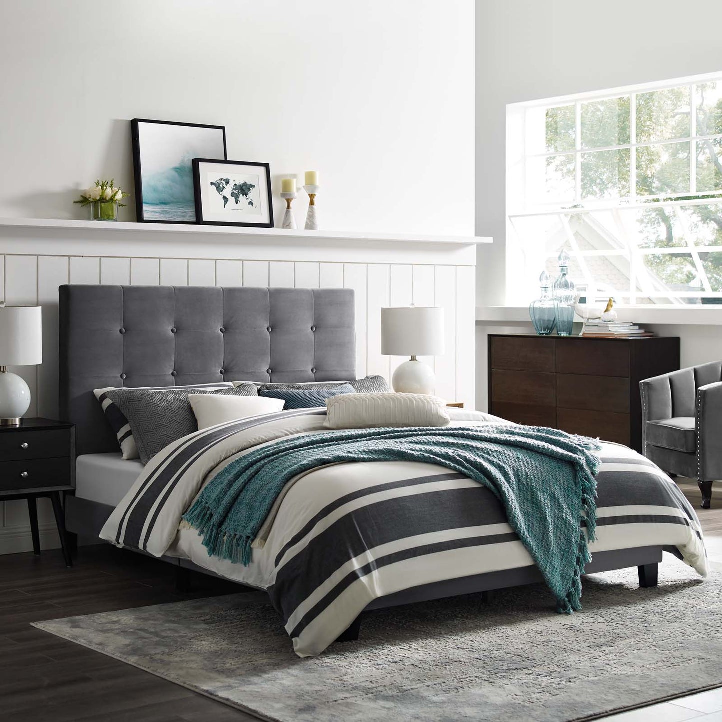 Grey tufted headboard bed with striped duvet, teal knit throw, white walls, nightstands, and sunlit window.