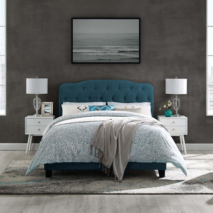 Teal blue tufted upholstered bed with white nightstands and glass lamps; ocean-photo art, blue floral duvet, gray throw.