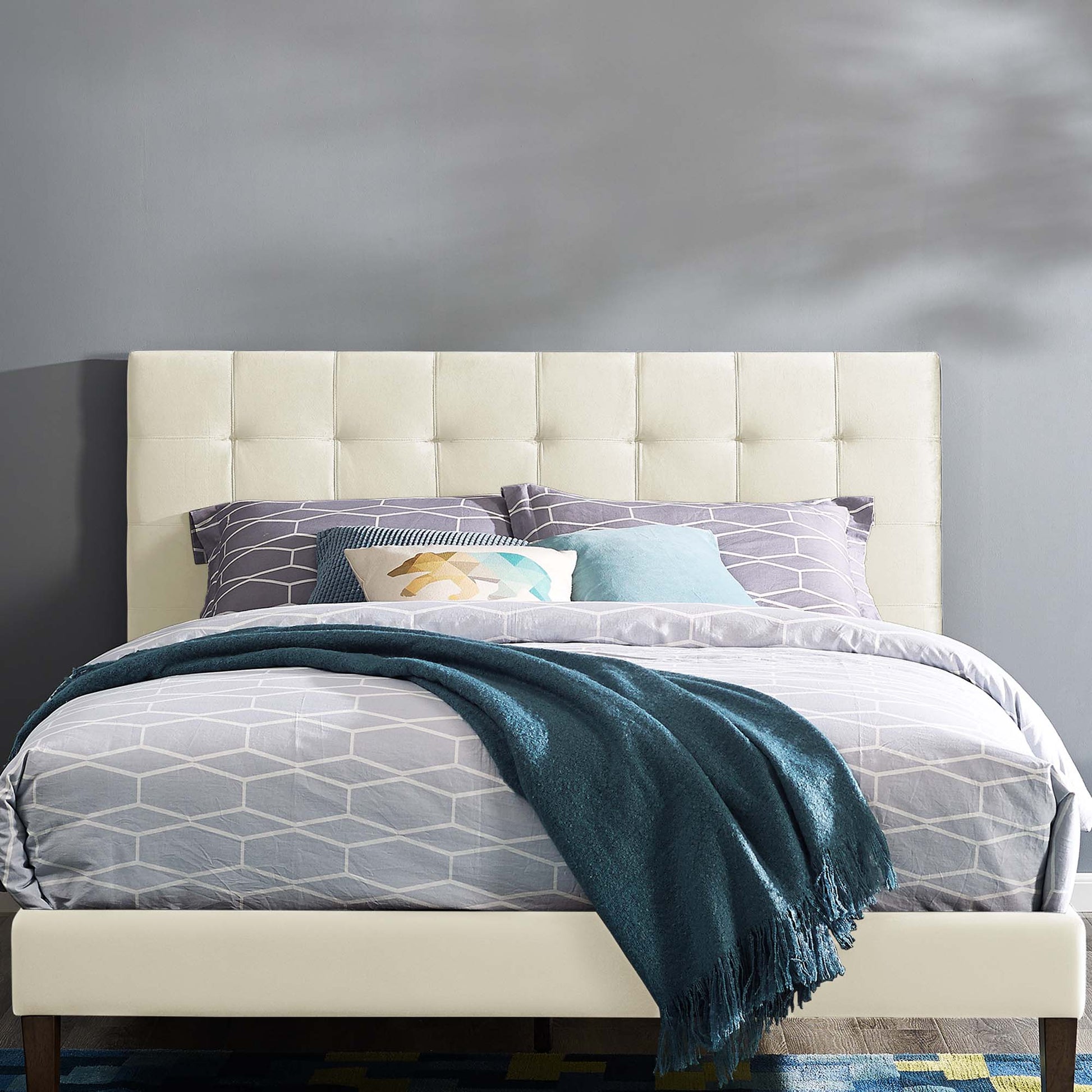 Ivory tufted upholstered headboard with a cushioned panel, shown with gray geometric bedding, teal throw, and lavender and aqua pillows.