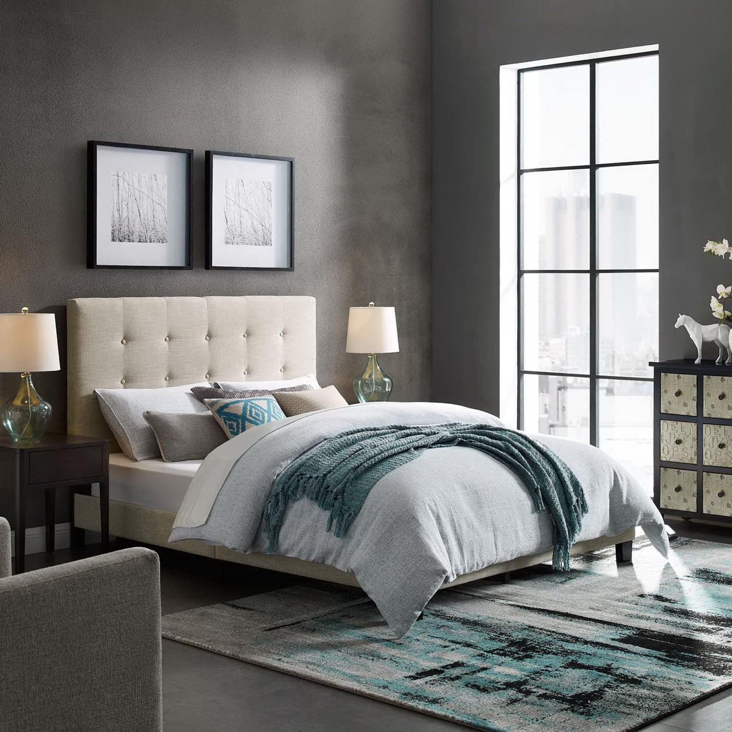 Beige tufted upholstered bed with gray bedding and teal throw, dark walls, two nightstands & glass lamps, large window