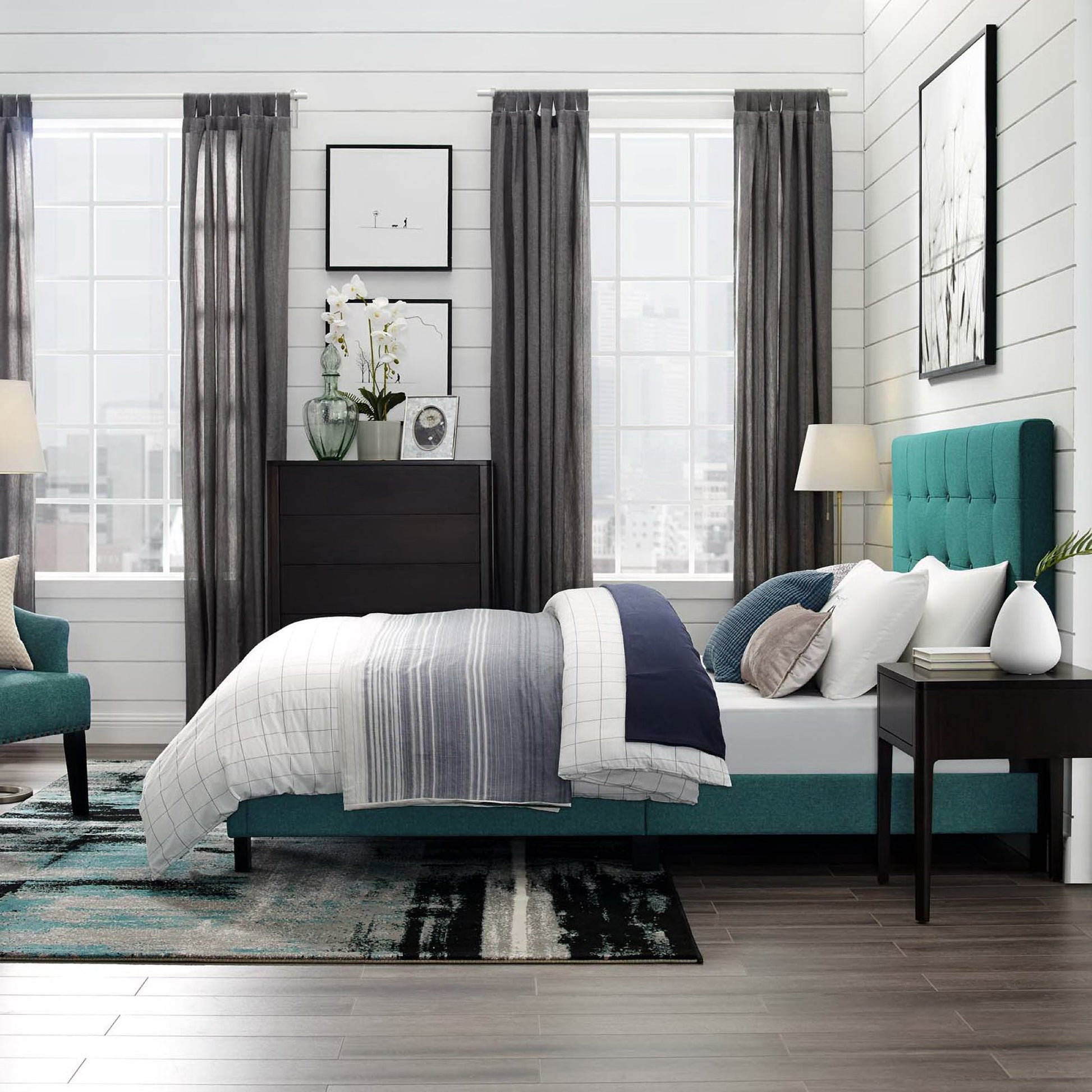 Teal upholstered platform bed with white-gray bedding, dark wood dresser, and gray curtains in a modern bedroom.