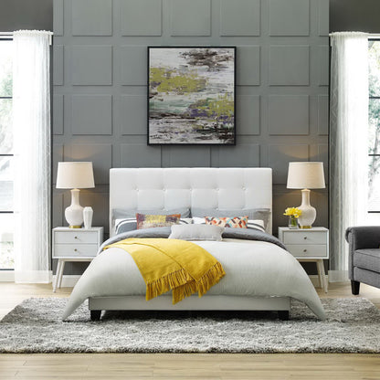 White tufted fabric queen platform bed with gray paneled wall, yellow throw blanket, matching nightstands & lamps, abstract wall art.