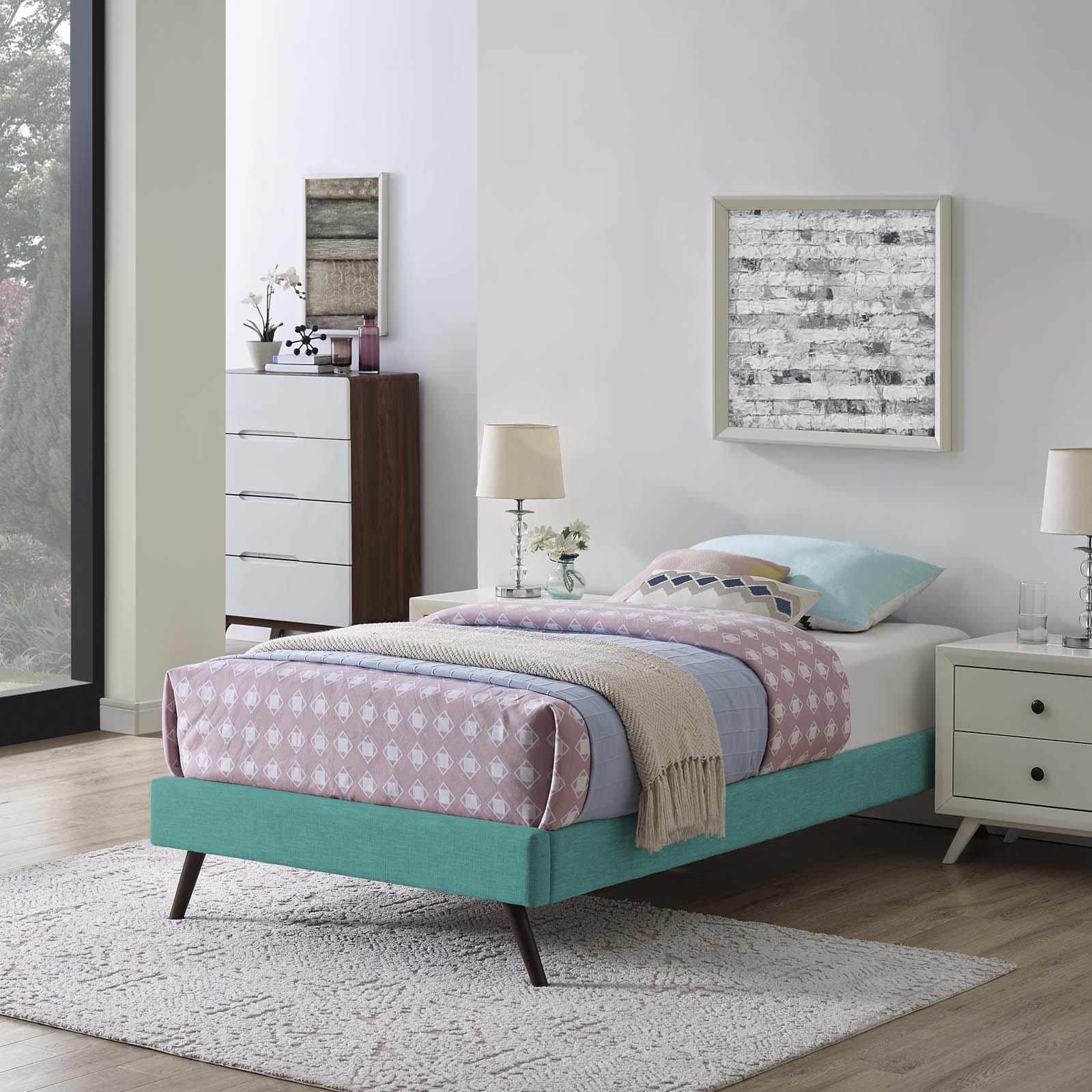 Teal fabric twin bed frame with round splayed legs, pink diamond quilt, light blue sheets, beige throw, white nightstands.