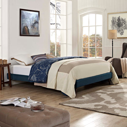 Teal upholstered bed frame with beige duvet and navy quilt, beige tufted ottoman, light wood floor in a bright coastal bedroom.