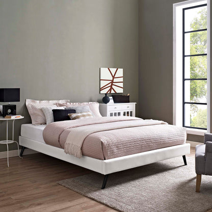 White vinyl king bed frame with round splayed legs in a modern bedroom, blush quilt, pillows, nightstand, large window.