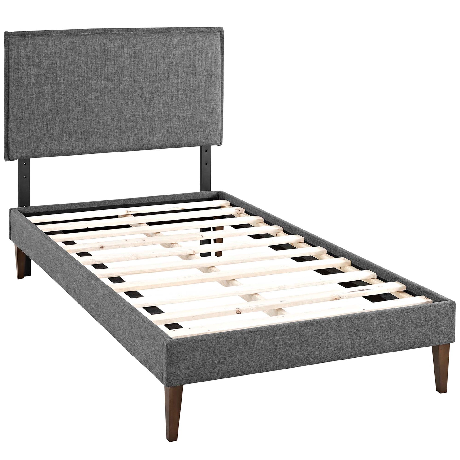 Gray fabric upholstered platform bed with tall padded headboard, slatted wooden base and squared tapered legs.