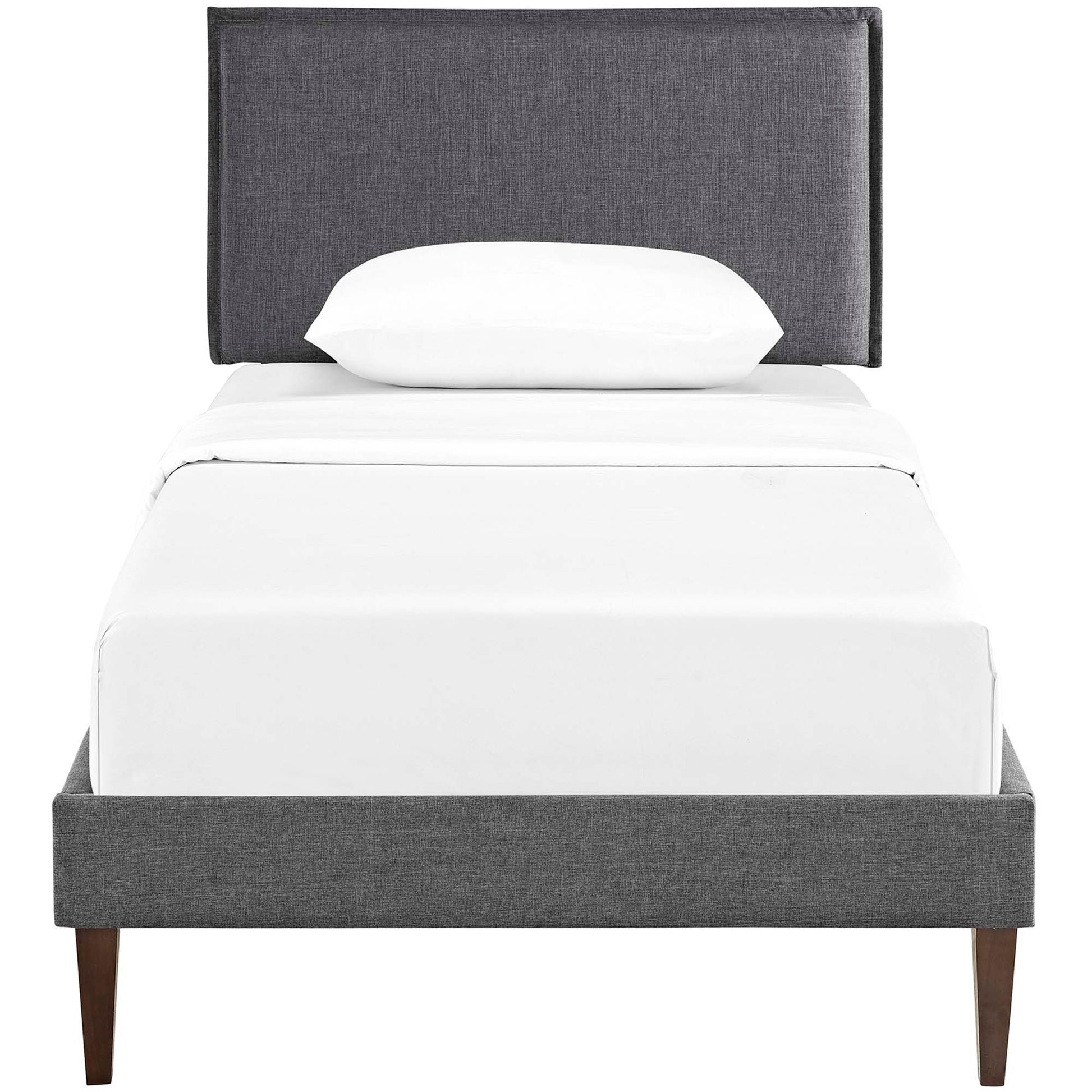 Gray upholstered platform bed with tall headboard, white sheets and pillow, tapered wood legs.