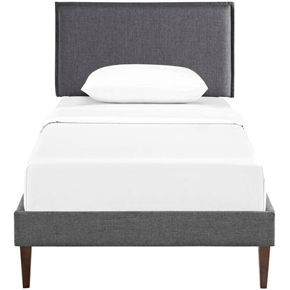 Gray upholstered platform bed with tall headboard, white sheets and pillow, tapered wood legs.