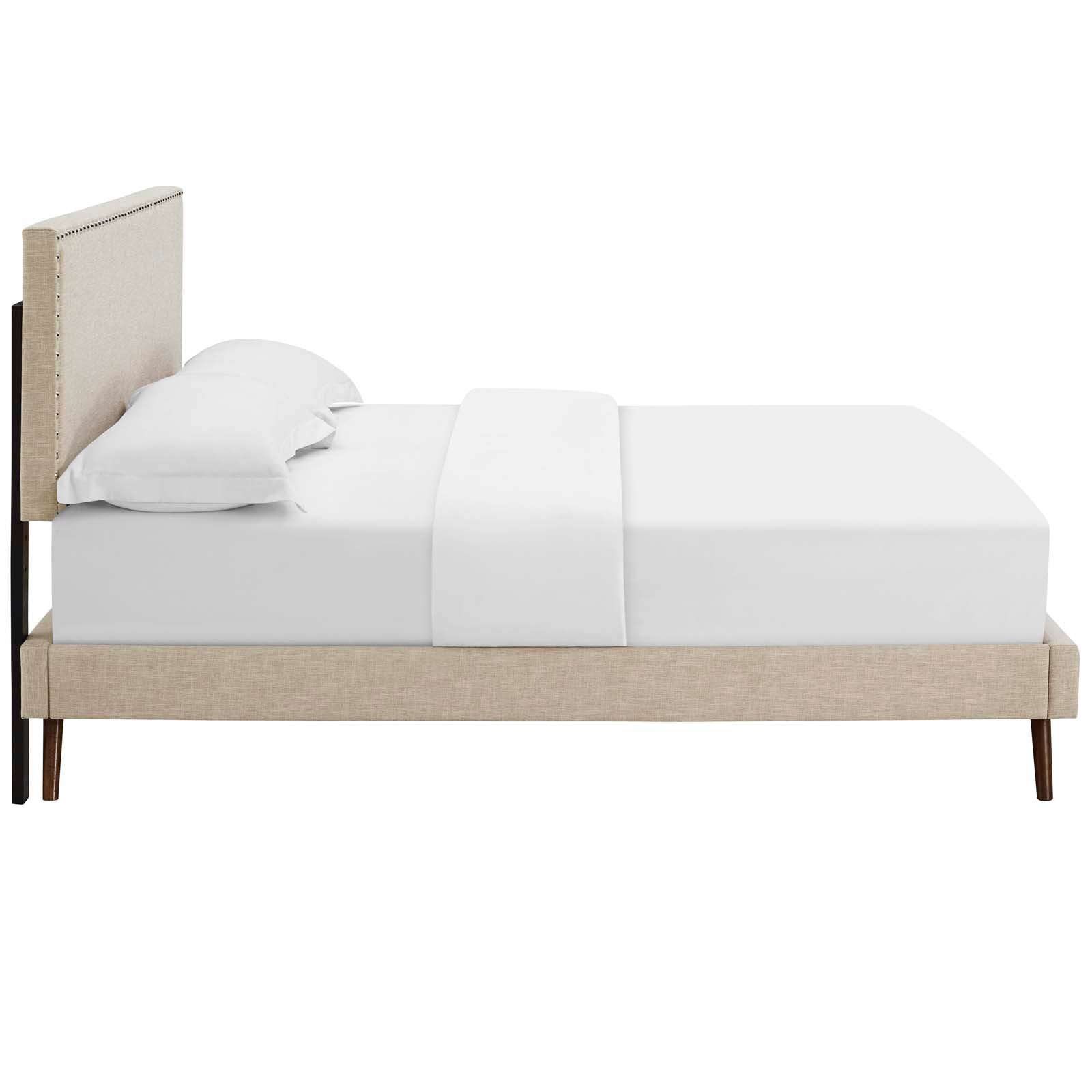 Beige fabric queen platform bed with a tall padded headboard and nailhead trim, round splayed legs, and white bedding.