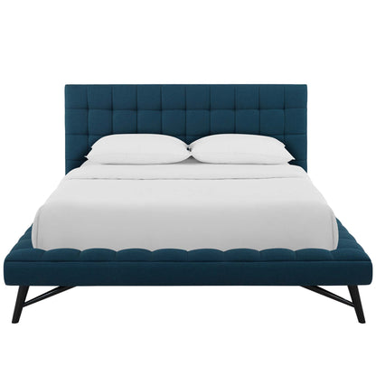Blue tufted upholstered platform bed with low footboard, angled black metal legs, & white bedding.