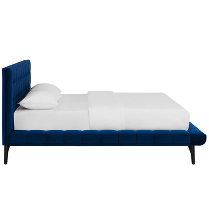 Navy blue velvet tufted platform bed with tall headboard, white sheets & pillows, black tapered legs.