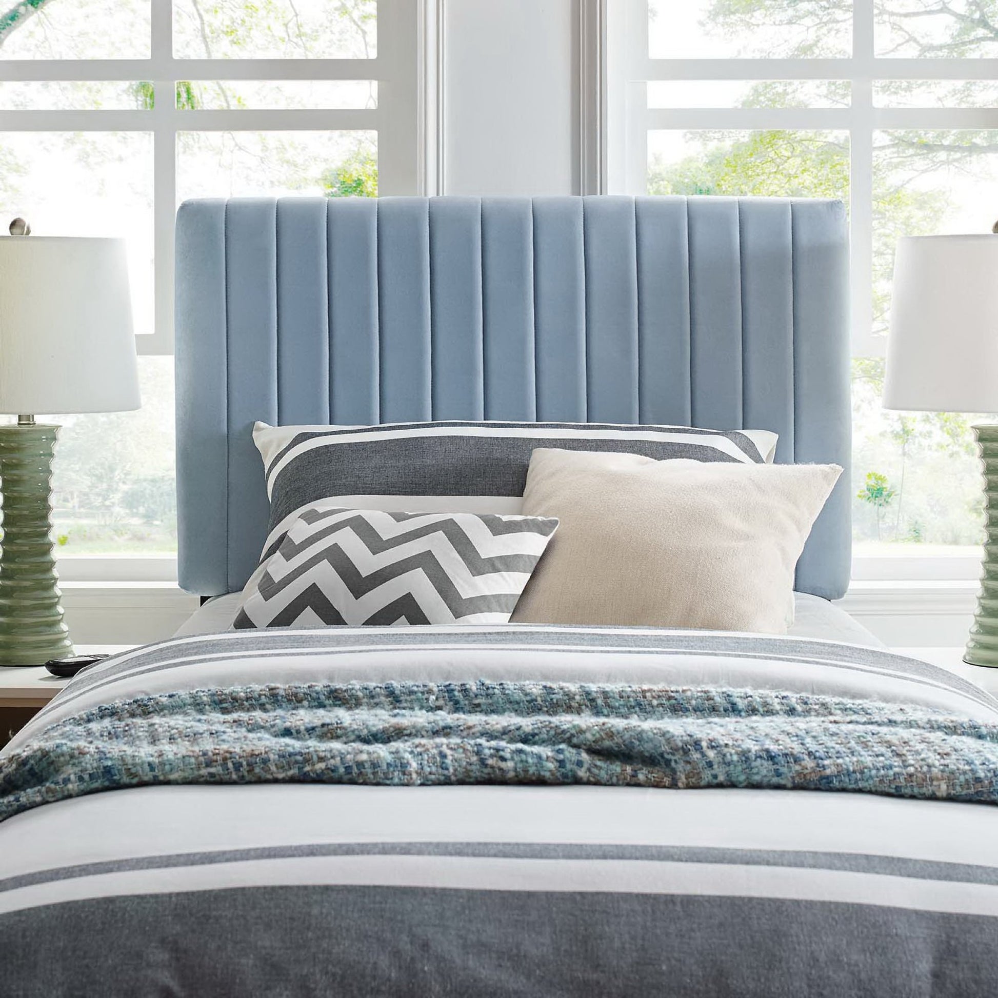 Soft blue velvet twin headboard with vertical channels, gray-blue bedding, chevron gray pillow, beige pillow, and textured throw.