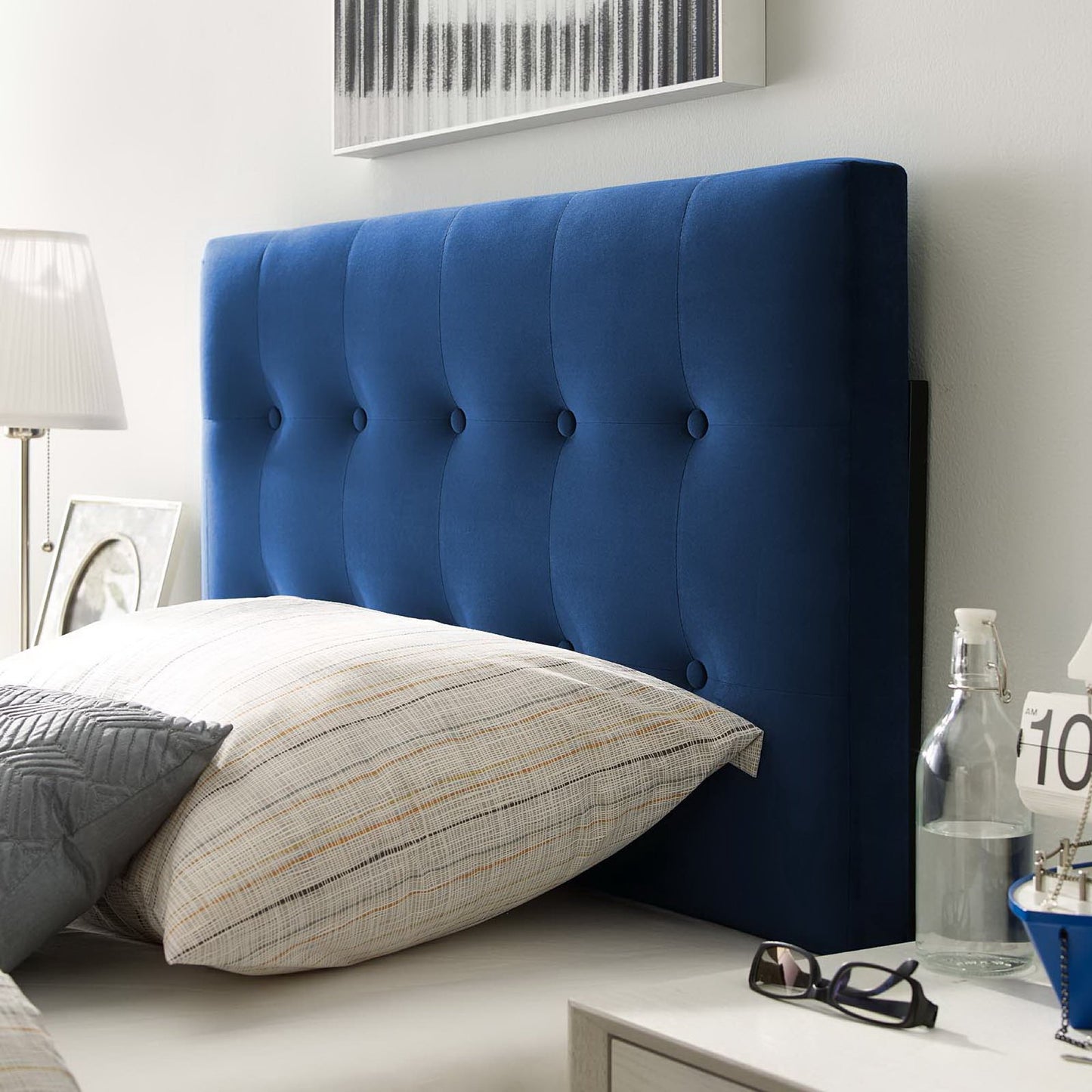 Navy blue tufted upholstered headboard with buttons, white bedding, and bedside lamp on a light bedroom wall.