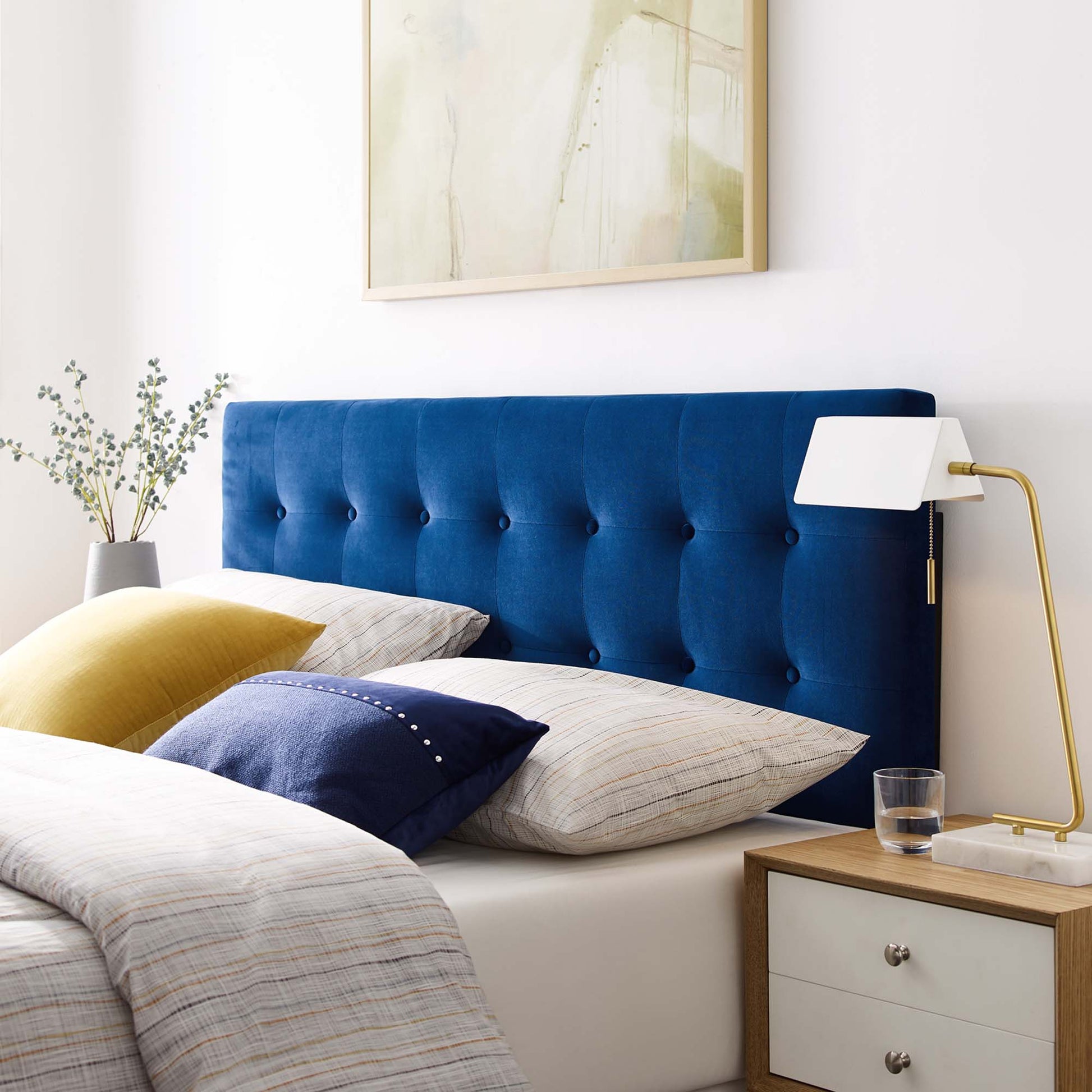 Navy velvet tufted headboard with plaid bedding, yellow & navy cushions, wooden nightstand, gold arc lamp.