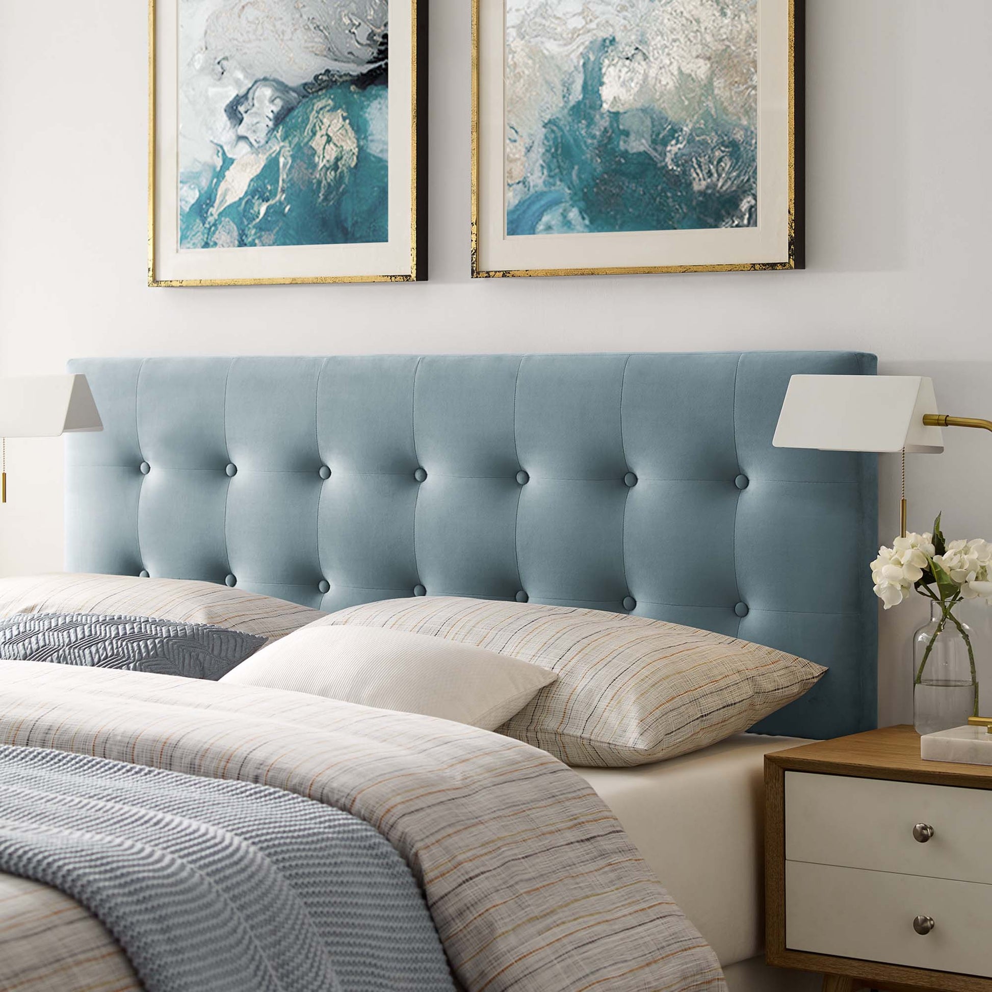Blue tufted upholstered queen headboard with beige striped bedding and gold-framed abstract art above.
