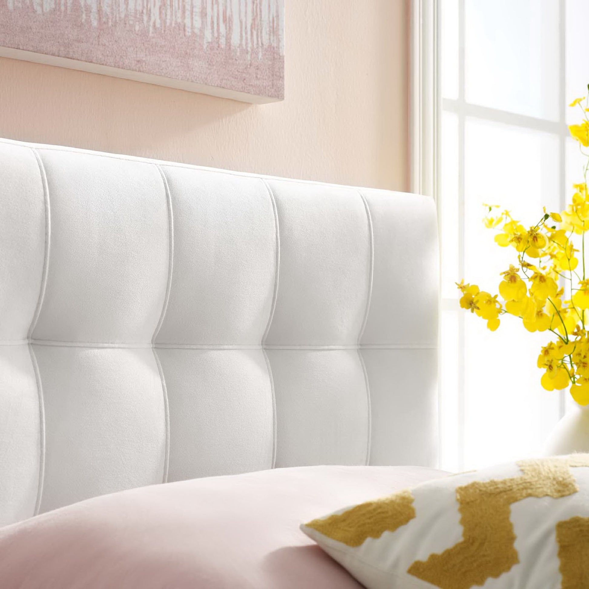 White tufted upholstered headboard against a peach wall, with pink bedding and yellow floral decor by a sunlit window.