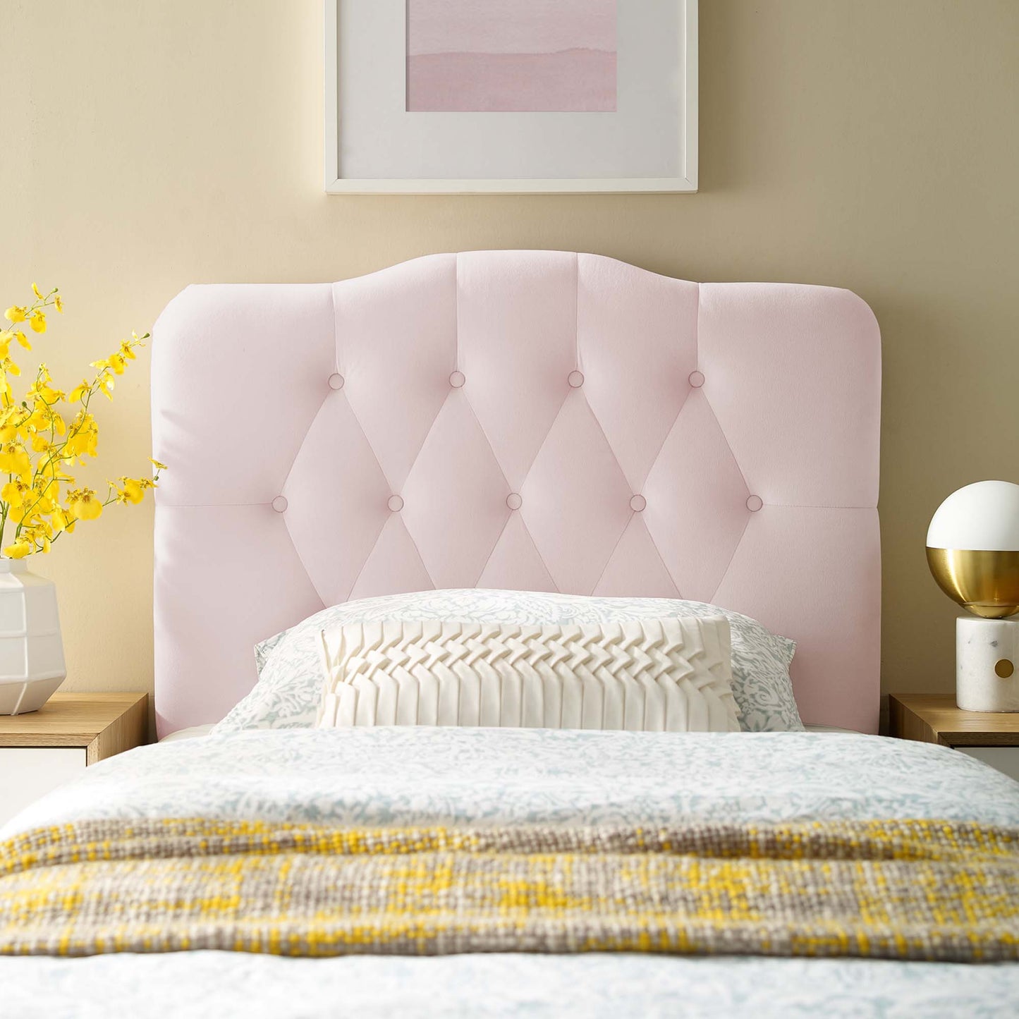 Soft pink tufted headboard with button details, white bedding, yellow throw, nightstands with lamp and vase of flowers