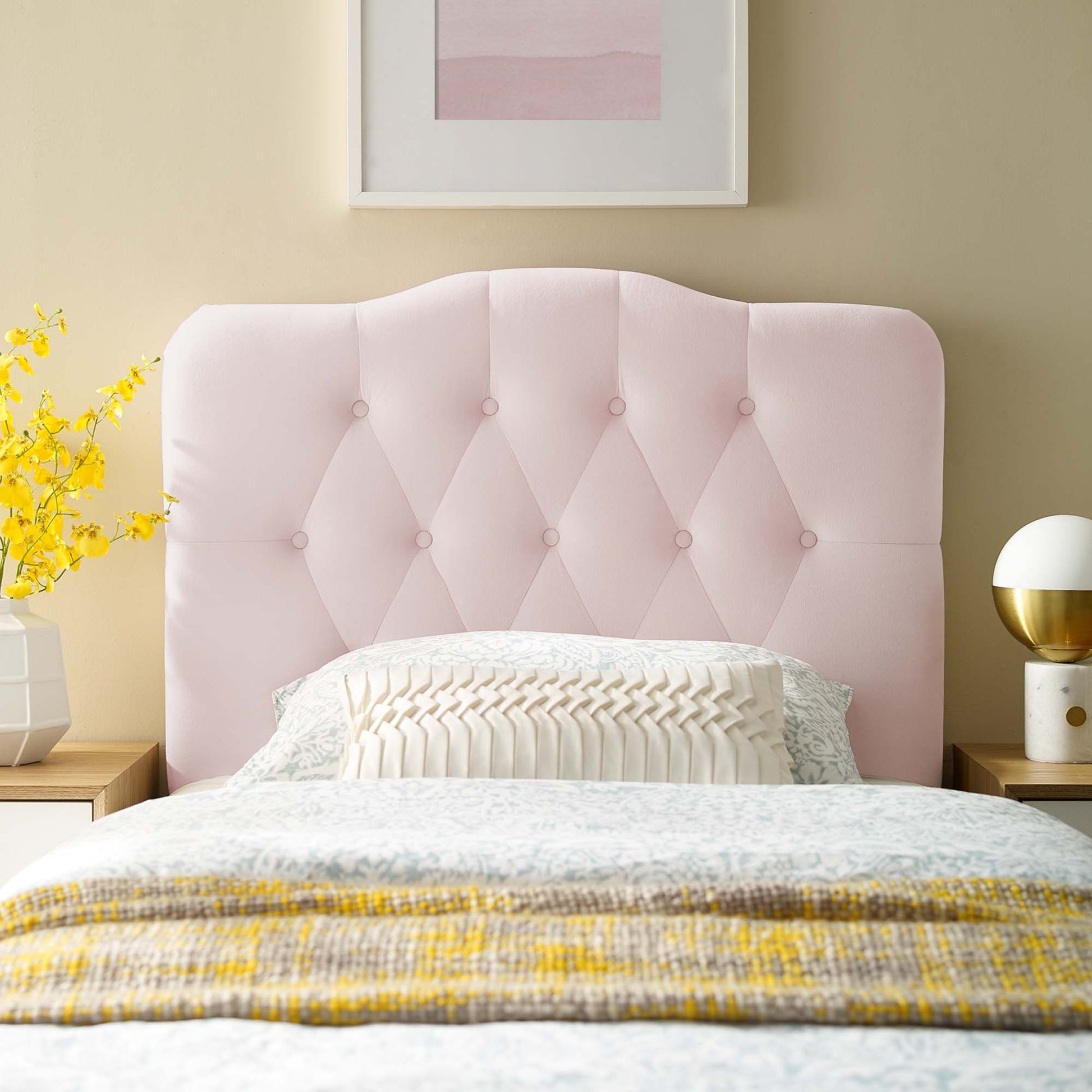Soft pink tufted headboard with button details, white bedding, yellow throw, nightstands with lamp and vase of flowers