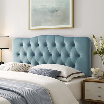 Modern coastal bedroom with a light blue tufted velvet headboard, white bedding, accent pillows, and a nightstand with lamp.