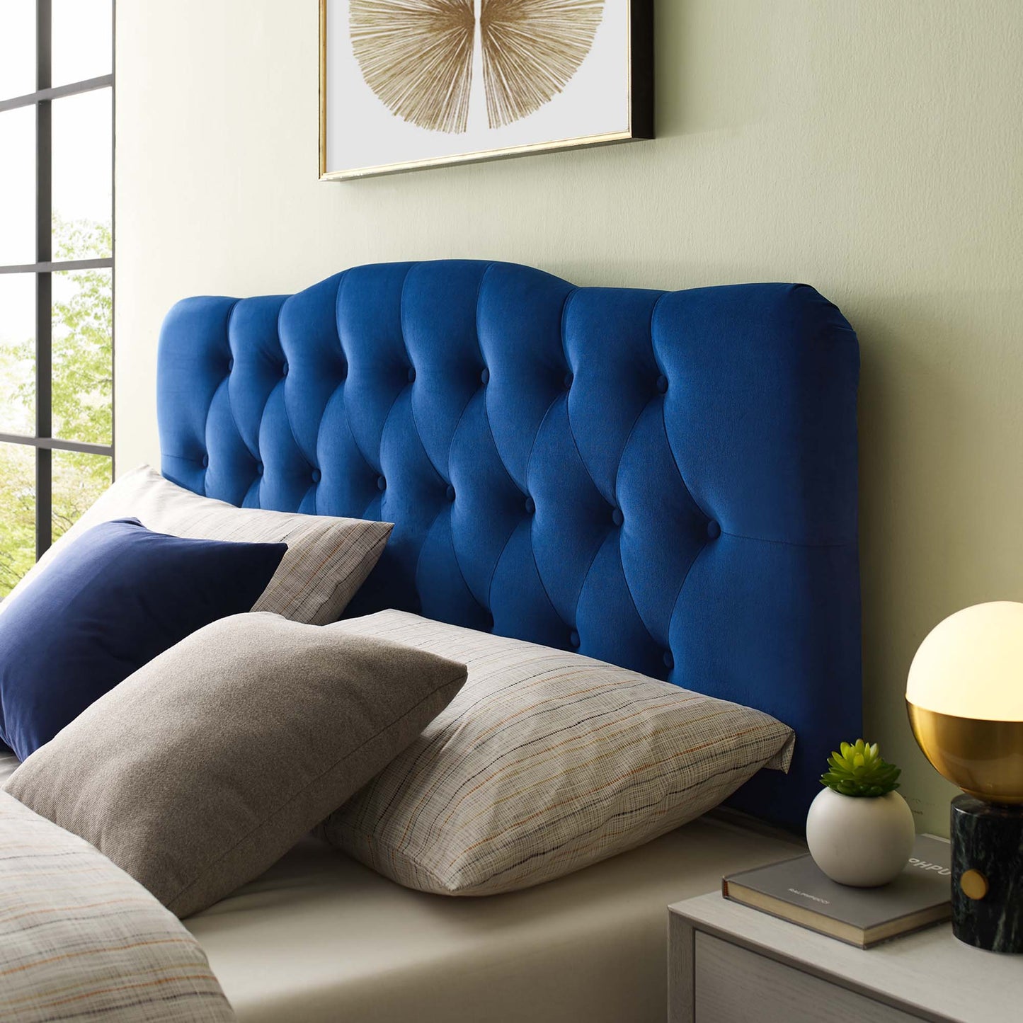Navy blue velvet tufted headboard with curved silhouette, beige bedding & pillows in a modern bedroom.