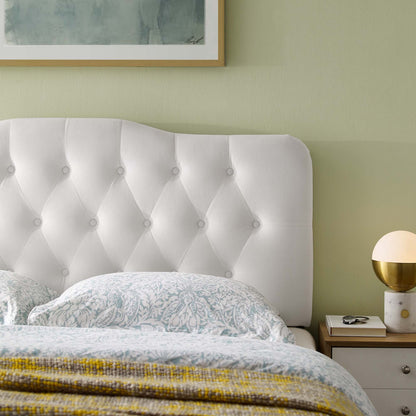 White tufted upholstered headboard with button detailing, light blue patterned bedding, pale green wall, nightstand with gold lamp.