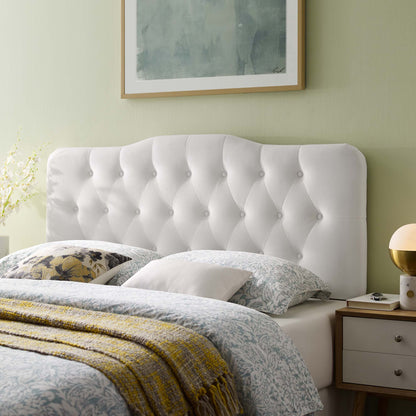 White tufted headboard with button details, pale green wall, blue patterned bedding, mustard throw, nightstand lamp.