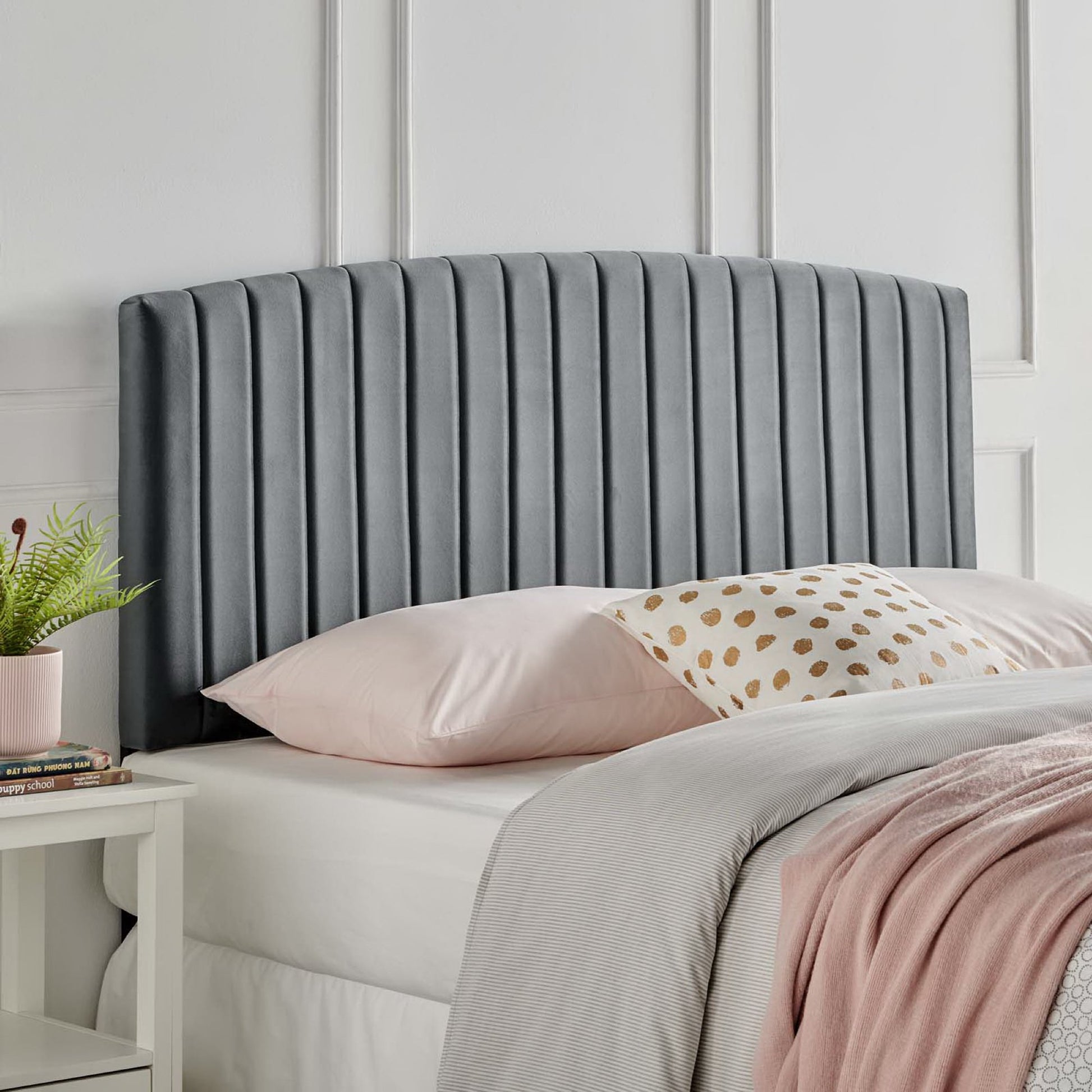 Dark gray upholstered headboard with vertical channel stitching atop a white bed with pink sheets.