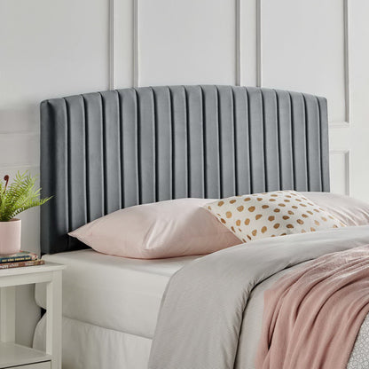 Dark gray upholstered headboard with vertical channel stitching atop a white bed with pink sheets.